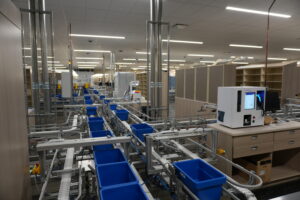 Factory production line with metal framework, conveyors, and blue plastic bins in a large warehouse workspace