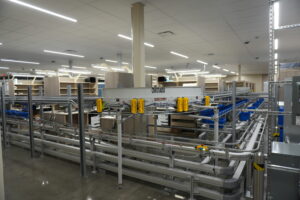 Industrial factory scene featuring automated conveyors, rails, and yellow safety components with shelving in the background