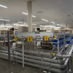 Automated warehouse with conveyor rails, yellow safety guards, and empty shelving in bright aisles.
