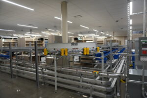 Automated warehouse with conveyor rails, yellow safety guards, and empty shelving in bright aisles.
