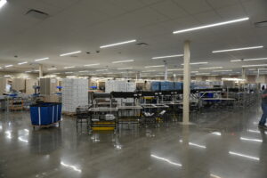Spacious distribution center with tall shelves, pallets, and a conveyor system under bright ceiling lights.