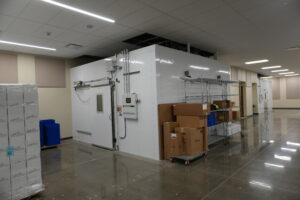 Industrial cold storage room with a white walk-in freezer and stacked boxes on the right.