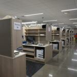 Packing station area in a warehouse with cubicle panels labeled Packing 16, computers and shelves nearby under bright fluorescent lights