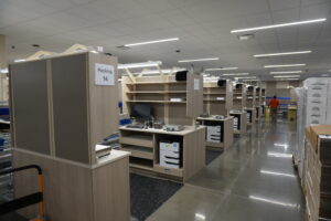 Packing station area in a warehouse with cubicle panels labeled Packing 16, computers and shelves nearby under bright fluorescent lights