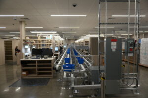Extended factory floor with conveyor system, blue bins, and assembly stations; a worker stands at left.