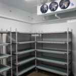 Empty industrial shelving in a cold storage room with a large refrigeration unit above the scene.