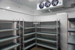 Empty industrial shelving in a cold storage room with a large refrigeration unit above the scene.