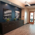 Office hallway with dark blue accent wall, two large black-and-white photos, and a dark cabinet with plants.