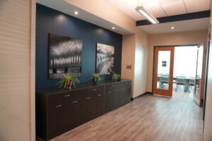 Office hallway with dark blue accent wall, two large black-and-white photos, and a dark cabinet with plants.