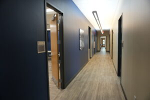 Narrow office hallway with dark blue walls, an open wooden door, and framed art along the corridor.