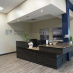 Norton Pharmacy reception desk area with dark wood counter, beige walls, and potted plants under a white ceiling.