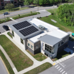 Aerial view of a police station with solar panels on the sloped roof, surrounded by roads, parking and green lawn areas.