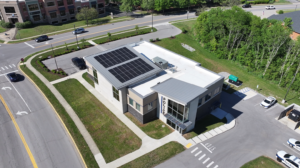 Aerial view of a police station with solar panels on the sloped roof, surrounded by roads, parking and green lawn areas.
