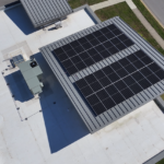 Aerial view of a flat commercial roof with a large solar panel array and a rooftop HVAC unit nearby.