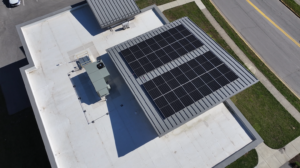 Aerial view of a flat commercial roof with a large solar panel array and a rooftop HVAC unit nearby.