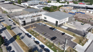 Aerial view of a modern industrial building with a large parking lot and nearby roadways.