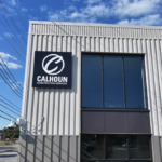 Modern gray metal building facade with a black Calhoun Construction Services sign and large window.