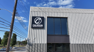 Modern gray metal building facade with a black Calhoun Construction Services sign and large window.