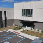 Exterior view of a modern office building with blue-accessible parking spaces and a wheelchair-accessible path to the entrance.